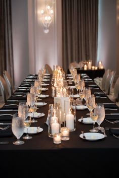 a long table is set with white candles and black linens for an elegant dinner