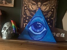 there is a blue pyramid with an eye in it and two skulls next to it