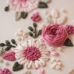 some pink flowers and green leaves are on a white table cloth with bead work