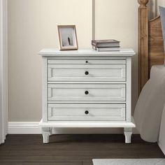 a white chest of drawers sitting on top of a wooden floor next to a bed