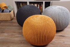 three knitted balls sitting on top of a wooden floor next to a book shelf