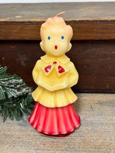 a yellow and red figurine sitting on top of a table next to a pine tree