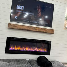 a black dog laying on top of a bed in front of a tv mounted above a fireplace