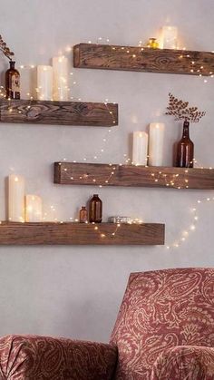 three wooden shelves with candles on them and some lights hanging from the wall behind them