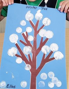 a young boy holding up a paper cut out of a tree with the words winter tree written on it