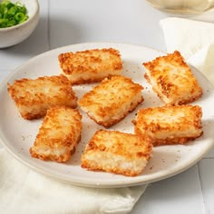 several pieces of breaded food on a white plate next to a bowl of salad