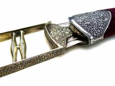 a silver knife and some other items on a white surface with a red velvet belt