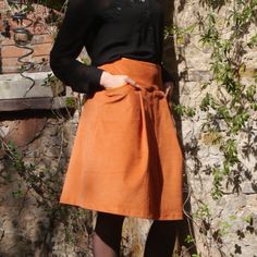 a woman standing in front of a stone wall wearing an orange skirt and black shirt