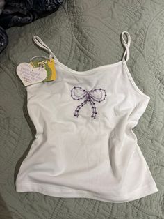 handmade beaded + embroidered bow on a white cami top 🎀 hand embroidered on white cami cropped tank top by me!! this one's for the coquette girlies <3  this listing has different color options while my previous one just had the pink :) White Bow Tank Top For Summer, White Sleeveless Tank Top With Bow, Casual Tank Top With Bow Straps, Summer Fitted Tops With Ribbon, Fitted Summer Tops With Ribbon, Fitted Summer Tops With Ribbon Detail, Cute White Tank Camisole, Fitted Cotton Tops With Bow Straps, White Embroidered Cami Tank Top