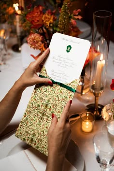 a person holding up a piece of paper on top of a table with candles and flowers