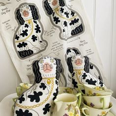 a white plate topped with cups and saucers covered in black and white cat designs