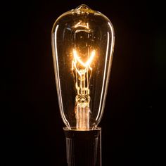 a light bulb that is on top of a glass stand with a black back ground