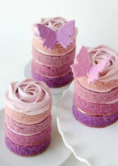 there are three cakes with pink frosting and purple icing on the cake plate