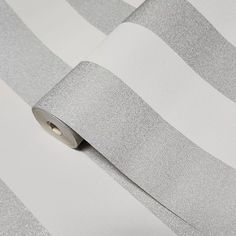 a roll of silver metallic foil on a white and grey striped wallpaper background with a circular hole in the middle