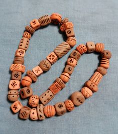 two necklaces made out of wooden beads on a blue cloth background, one has a cross and the other is a skull