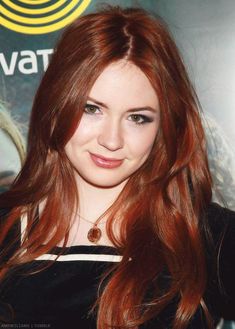 a beautiful young woman with long red hair posing for the camera in front of a movie poster