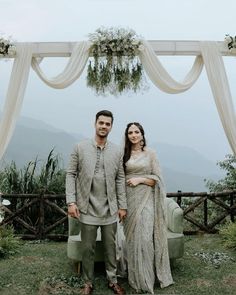 a man and woman standing next to each other in front of an arch with flowers on it