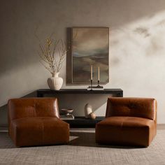 two brown chairs sitting next to each other in front of a painting on the wall