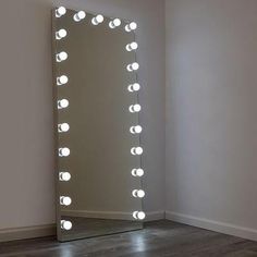 a large mirror with lights on it sitting in a room next to a wall and floor