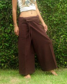 a woman standing in front of a hedge wearing wide legged pants and a crop top