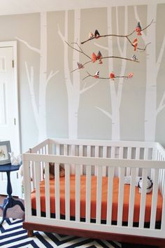 a baby's room with a white crib and trees painted on the wall