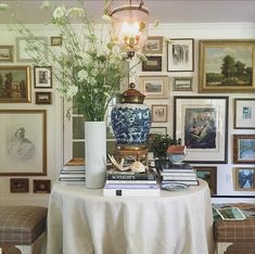 a table topped with books and vases filled with flowers next to pictures on the wall