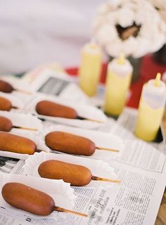 hotdogs on skewers sitting on top of a newspaper with candles in the background