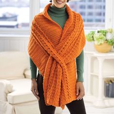 a woman wearing an orange knitted shawl in front of a white couch and window