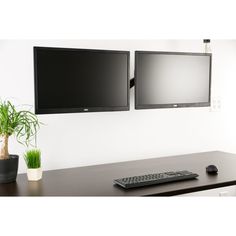 two flat screen tvs mounted on the wall above a desk with a keyboard and mouse