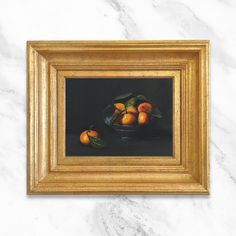 a painting of oranges in a glass bowl on a marble surface with gold frame