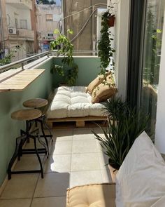 a small balcony with some plants on the windowsill and two stools next to it