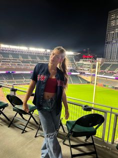 a woman standing on top of a baseball field next to empty chairs in front of a stadium