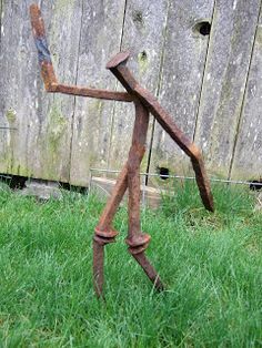 a metal sculpture is standing in the grass near a wooden fence and some green grass