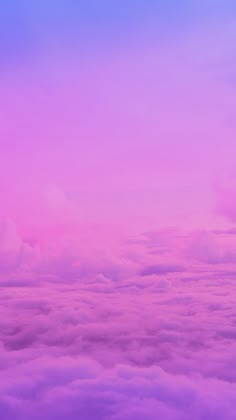 the view from an airplane looking down on some clouds and blue sky with pink hues