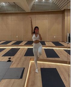 a woman is doing yoga in a large room with wooden flooring and lights on the ceiling