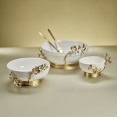 three white bowls with gold rims and spoons in the shape of flowers on them