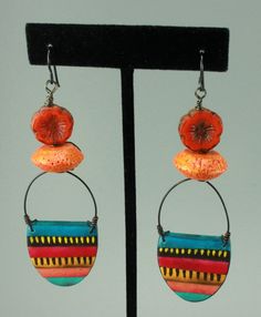 #1403, Painted Polymer Clay Charms by Holly Stultz are paired with Orange Coral and Czech Glass Flowers. Black toned Niobium Earwires finish off the design. The Niobium earwires can be changed at no charge to another color as featured in the photos...just let me know what you would like. Each earring hangs from the top of the earwire at 3.5 inches; from the bottom of the earwire 3.2 inches; and their width is 1 inch. Each earring is a very light weight of less that .15 ounces. Packaging & Shipping is included in the price listed. The last set of photos feature my jewelry gift boxes with appropriate colorful ribbon, the Niobium earwire colors, a display of what has been on my design table lately & other jewelry.  Please treat Chris Kaitlyn Jewelry like Wearable Art by keeping the item(s) aw Multicolor Vibrant Jewelry With Ear Wire, Artsy Multicolor Jewelry With Matching Earrings, Vibrant Multicolor Jewelry With Ear Wire, Vibrant Multicolor Earrings, Nickel-free Multicolor Artsy Earrings, Artsy Multicolor Nickel Free Earrings, Artsy Multicolor Nickel-free Earrings, Artistic Multicolor Earrings With Unique Variations, Artistic Multicolor Jewelry With Colorful Design