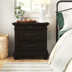 a bedroom with a bed, nightstand and basket on the floor next to it in front of a window