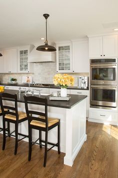 a large kitchen with white cabinets and black counter tops, two stools at the island