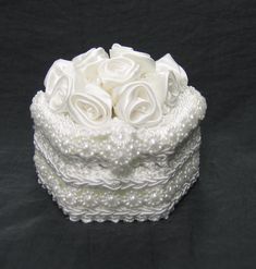 a white wedding cake with pearls and roses on top is sitting on a black background