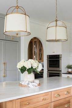 two lights hanging over a kitchen island with flowers in the center and an oven behind it