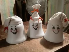 three white bells with faces painted on them sitting on a table next to a fan