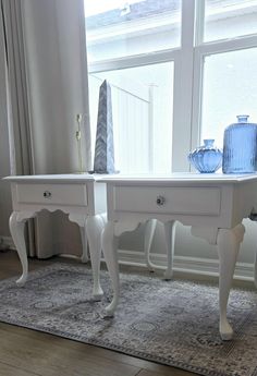 two white tables with blue vases on them in front of a large windowsill