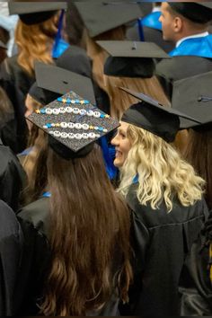 a group of people in graduation gowns and caps with beads on their hats are looking at each other