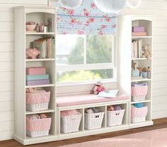 a white shelf filled with baskets next to a window covered in pink and blue curtains