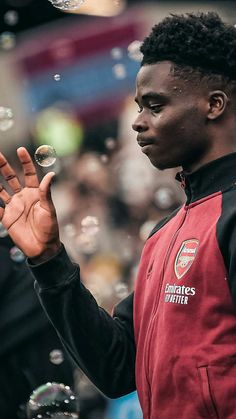 a man in a red jacket blowing bubbles on his hand and looking at the camera