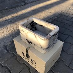 a white box sitting on top of a block of wood next to a brick road