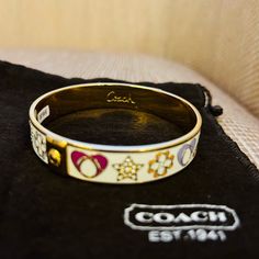 Coach Nwt Enamel And Gold Tone Cuff Bracelet With Sparking Gem Embellishments. Hearts, Flowers And Stars Encircle The Bracelet. Fits Most Med/Large. Includes Bag, Paper Pamphlet And 98.00 Sticker Tag On Interior Of Bracelet. Coach Adjustable Bangle, Adjustable Coach Bangle, Elegant Adjustable Enamel Bangle, White Enamel Bangle Jewelry, White Enamel Bangle, White Cuff Bangle For Gift, White Cuff Bangle As Gift, White Cuff Bangle Suitable As A Gift, Signature Bracelet