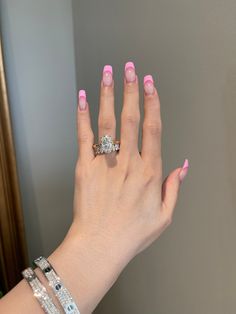 a woman's hand with pink nail polish holding a diamond ring