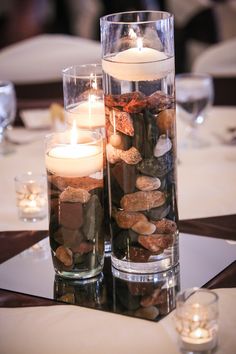 two clear vases filled with rocks and lit candles